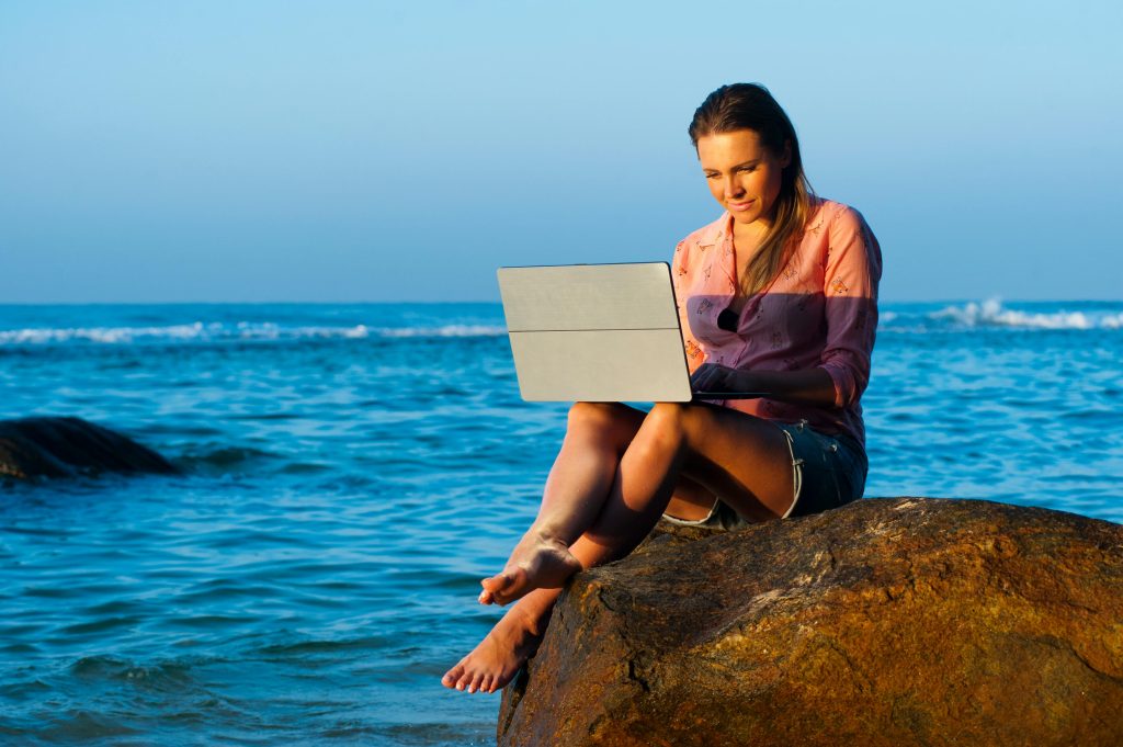 Formación online y trabajo remoto: mujer usando portátil en la playa, libertad geográfica